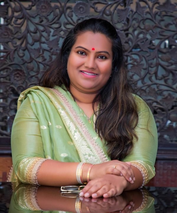 Mrs. Bhavnatai Bordikar, Chairperson, smiling, seated at a table in a green saree