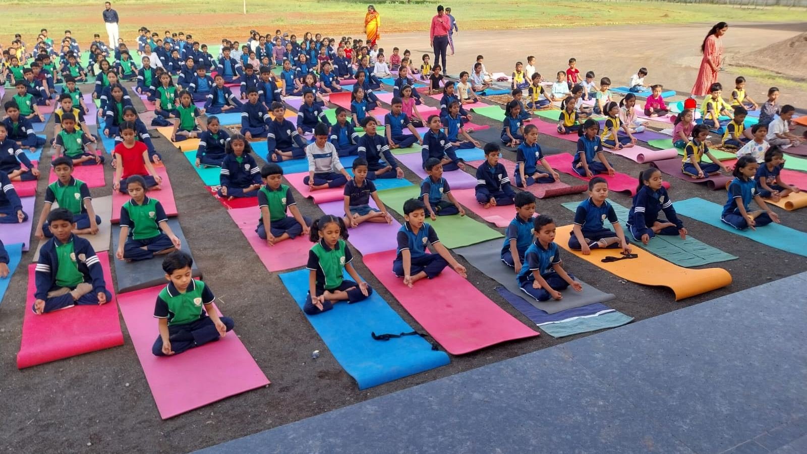 Rows of students practising yoga on colourful mats on the school ground